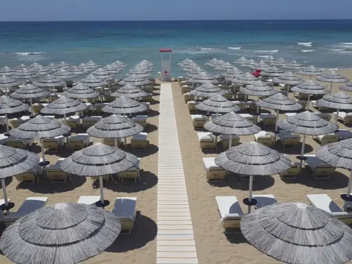 Filettato di ombrelloni di paglia e lettini sulla sabbia dorata, con il mare azzurro sullo sfondo. Un paradiso a Presicce Lido Marini.