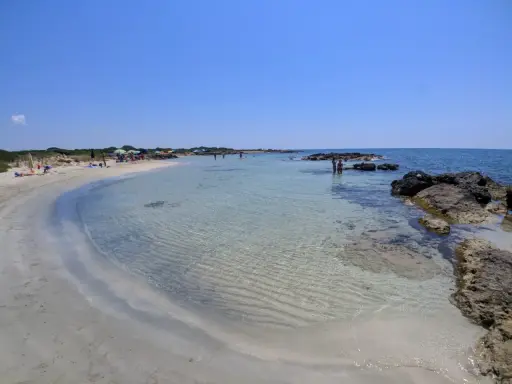 Spiaggia di sabbia bianca e mare cristallino a Marina di Salve, con scogli e persone che si godono il sole.