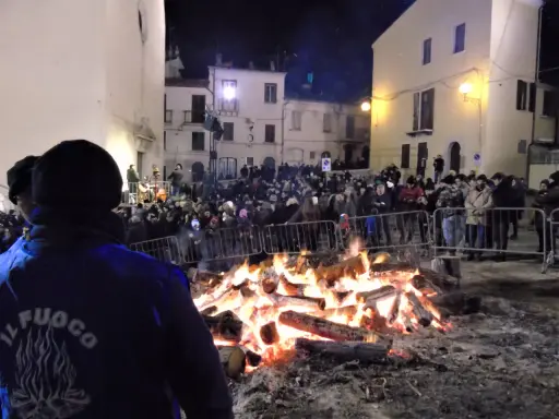 Grande falò nella piazza per la festa della birra Sant'Antonio Abate. La folla ammira le fiamme mentre un gruppo suona musica.