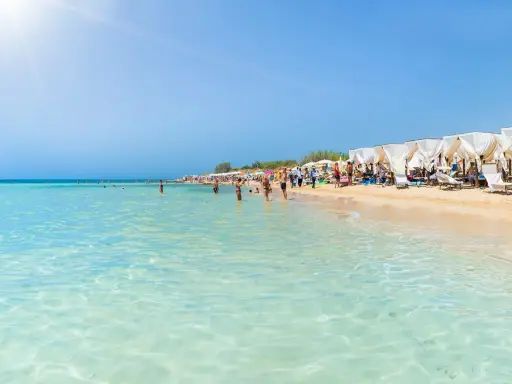 Spiaggia pugliese con acque cristalline e lettini sotto gazebo bianchi, ideale località mare Puglia per famiglie.