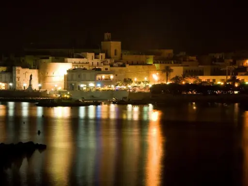 Otranto di notte: luci, castello e riflessi sull'acqua. La città si anima, pronta per le discoteche estive.