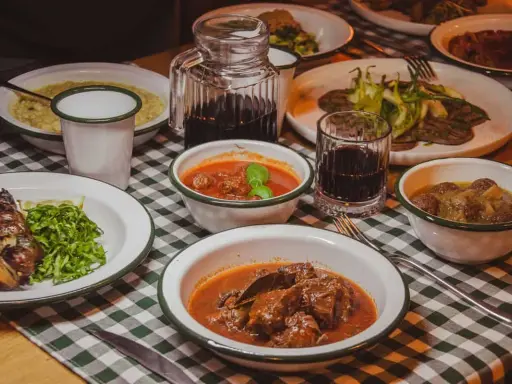 Tavola imbandita in una trattoria tipica salentina con vari piatti di carne e contorni, accompagnati da vino rosso.