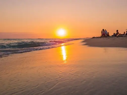 Tramonto dorato sulla spiaggia di Ugento, Salento. Famiglie rilassate sulla sabbia mentre il sole si specchia sul mare calmo.