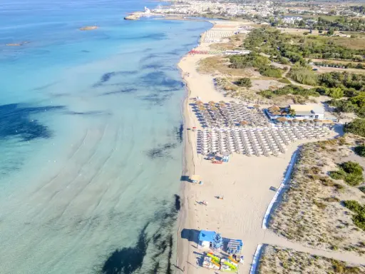 Spiaggia di Torre San Giovanni con ombrelloni e lettini, mare cristallino e vegetazione mediterranea.