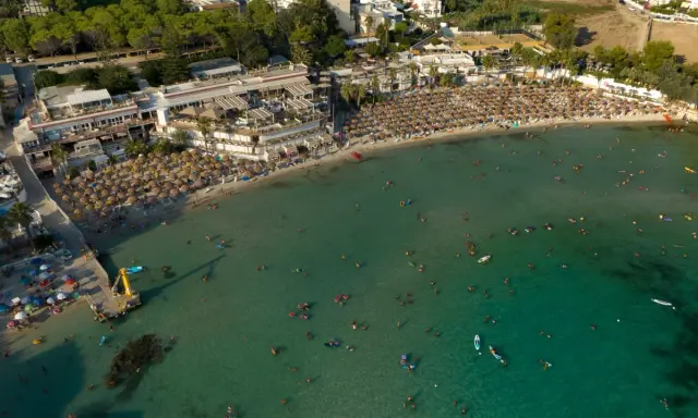 Vista aerea di una spiaggia affollata con ombrelloni e persone che nuotano nel mare cristallino, una delle spiagge più belle del mare di Taranto.