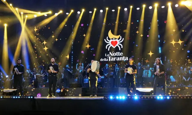 Artisti sul palco con tamburelli, orchestra e luci scintillanti per la sagra della taranta.