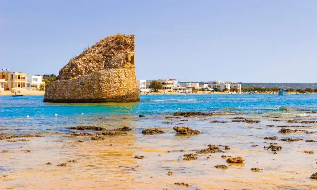La torre pali di Lido Marini, con il mare cristallino e le case bianche sullo sfondo, evoca un'estate senza fine.