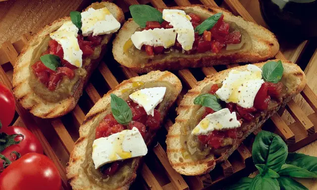 Bruschetta supersano con melanzane, pomodori e mozzarella fresca, guarnita con basilico e un filo d'olio.