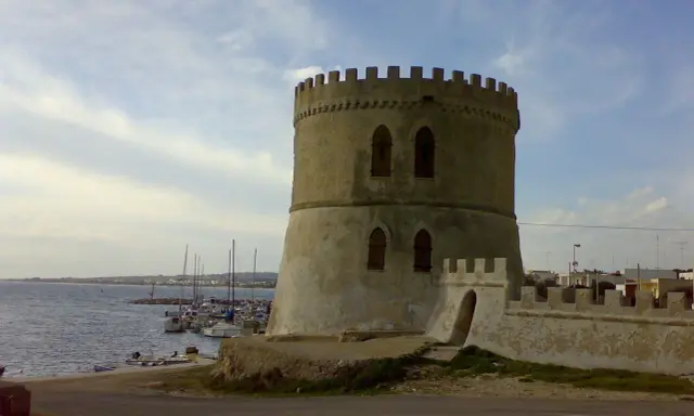 Torre Vado centro storico: antica torre circolare con merlature, affacciata sul mare con barche ormeggiate.