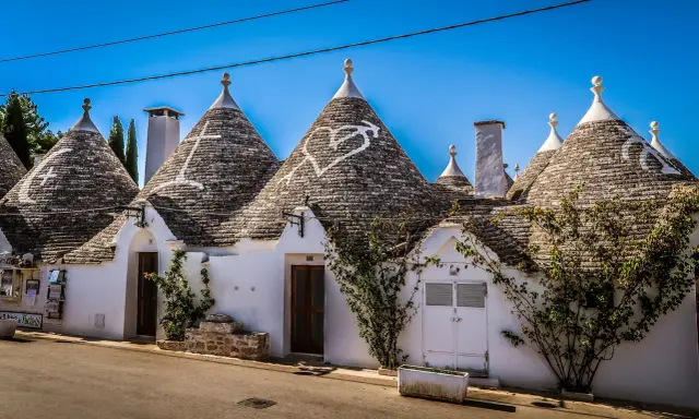 Trulli bianchi con tetti conici in pietra, un cuore disegnato su uno di essi, in un borgo tra i più belli d'Italia in Puglia.