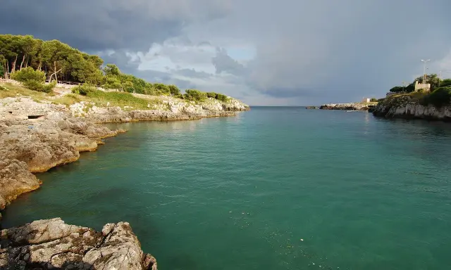 Baia rocciosa con acqua cristallina, alberi sulla costa. Un paesaggio che evoca i modi di dire salentini, come "fare la bella vita".
