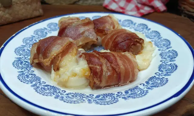 Involtini di interiora pugliesi avvolti in pancetta croccante, serviti su un piatto bianco con decorazioni blu.