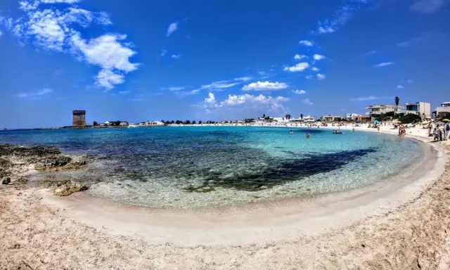 Spiaggia incantevole nel Salento ionico, con acque cristalline, sabbia dorata e un'antica torre di avvistamento.