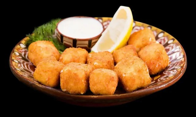 Croccanti cubetti di ricotta fritta salentina dorati, serviti su un piatto decorato con limone, salsa bianca e aneto.