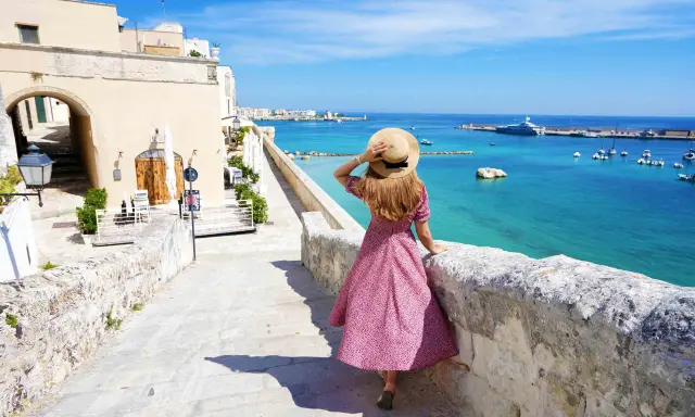 Una donna con cappello di paglia ammira il mare turchese e il porto di Otranto. Scopri cosa vedere in questo gioiello pugliese.