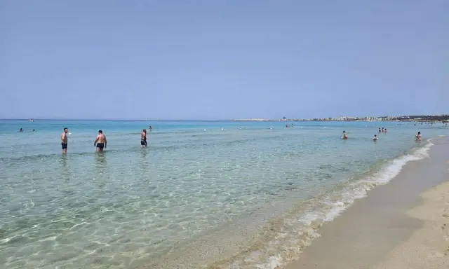 Persone in acqua cristallina vicino alla spiaggia di Gallipoli paese. Il mare calmo riflette il cielo azzurro.