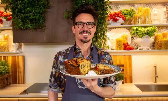 Chef sorridente con un piatto di torta salata, ispirata alle ricette leccesi, con pomodorini e basilico sullo sfondo.