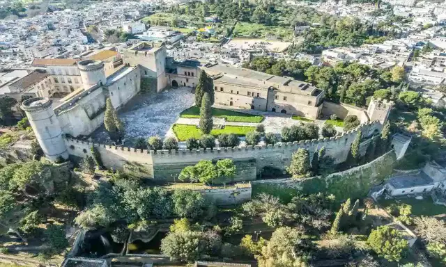 Castello normanno con torri rotonde e mura merlate, ideale per scoprire dove andare a Pasquetta in Puglia, circondato da verde e un borgo.