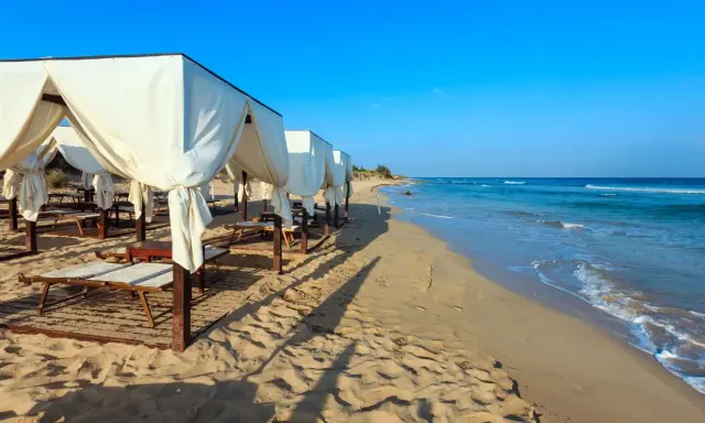 Spiaggia di Pescoluse con gazebo bianchi e lettini, mare azzurro e sabbia dorata. Ecco cosa vedere a Pescoluse per una vacanza da sogno.
