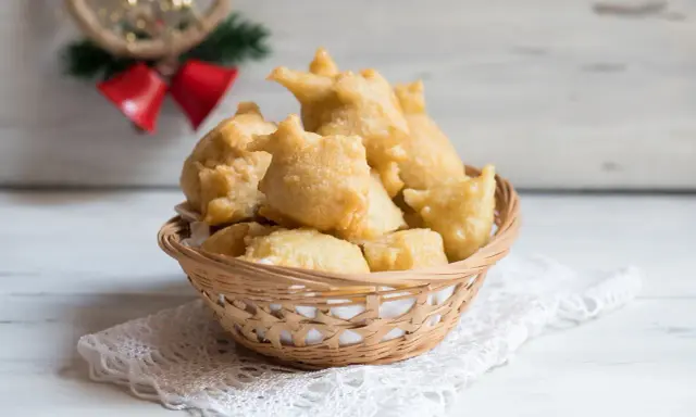 Cesto di pittula salentina dorata, un dolce fritto tipico delle feste, su un pizzo bianco.