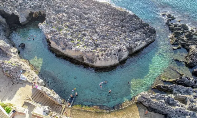 Tricase cosa vedere: una baia rocciosa con acque cristalline e persone che nuotano. Un luogo incantevole per godersi il mare.