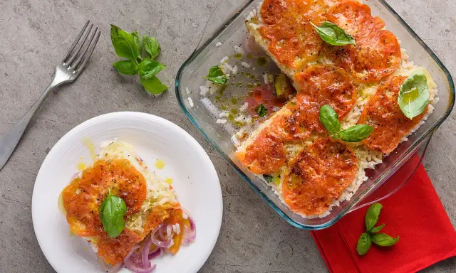 Una fetta di tiella pugliese di verdure, con riso, pomodori e cipolle rosse, guarnita con basilico fresco.
