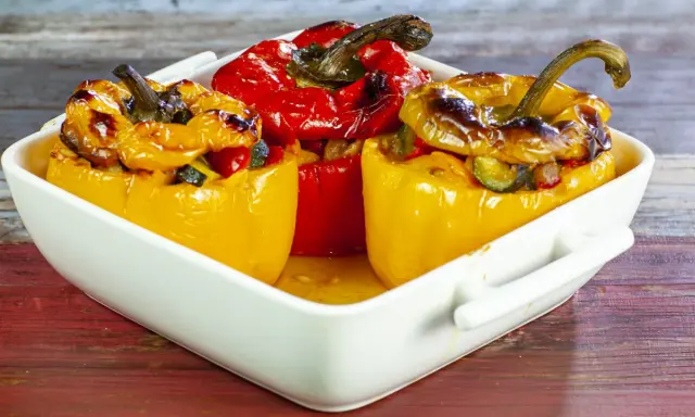 Peperoni ripieni di riso alla salentina, dorati e invitanti, in una teglia bianca su un tavolo di legno.