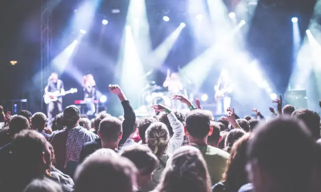 Folla entusiasta a un concerto in Puglia il 1 maggio, con luci intense e musicisti sul palco.