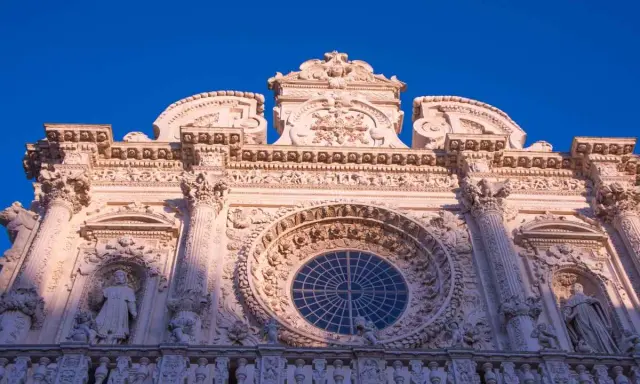 Facciata barocca di Lecce, con un grande rosone centrale e statue. Un esempio di cosa vedere a Lecce, tra arte e storia.