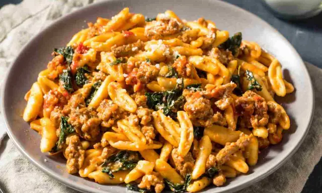Un piatto di pasta con salsiccia sbriciolata, verdure e formaggio grattugiato, un sapore autentico dei primi piatti foggiani.