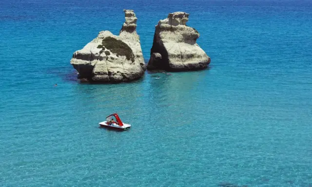 Due faraglioni bianchi emergono dal mare cristallino, con una pedalò che naviga vicino alla spiaggia dell'orso.