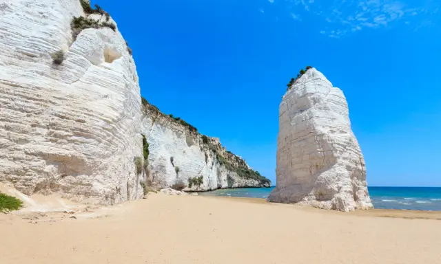 Spiagge sabbiose Puglia: scogliere bianche imponenti si affacciano su un mare azzurro e una distesa dorata.