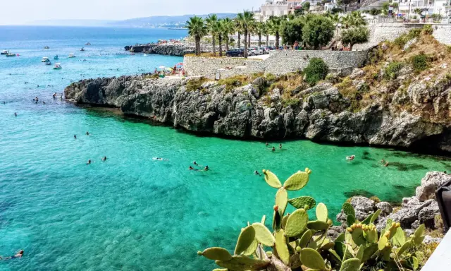 Splendida baia pugliese con acque cristalline e scogliere rocciose. Gente che nuota e si gode il sole, un vero paradiso per chi ama il **puglia mare**.