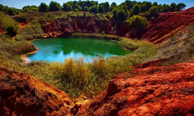 Un suggestivo lago di bauxite in Puglia, con acque verdi smeraldo circondate da rocce rosse e vegetazione lussureggiante.