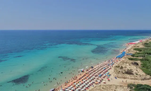 Spiaggia affollata con ombrelloni colorati e acque cristalline, le Maldive della Puglia dove si trovano per godersi il sole e il mare.