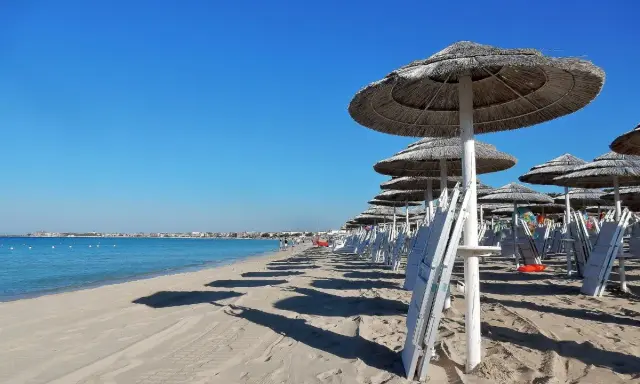 Ombrelloni di paglia e lettini bianchi sul lungomare Torre Lapillo, con il mare azzurro e il cielo limpido.