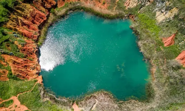 Laguna turchese in un cratere dalle rocce rosse, un paesaggio surreale delle cave di bauxite Otranto.