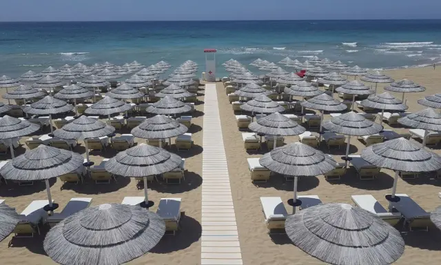 Filettato di ombrelloni di paglia e lettini sulla sabbia dorata, con il mare azzurro sullo sfondo. Un paradiso a Presicce Lido Marini.
