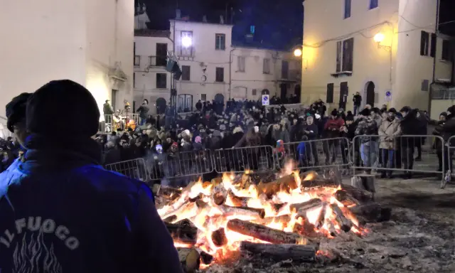 Grande falò nella piazza per la festa della birra Sant'Antonio Abate. La folla ammira le fiamme mentre un gruppo suona musica.