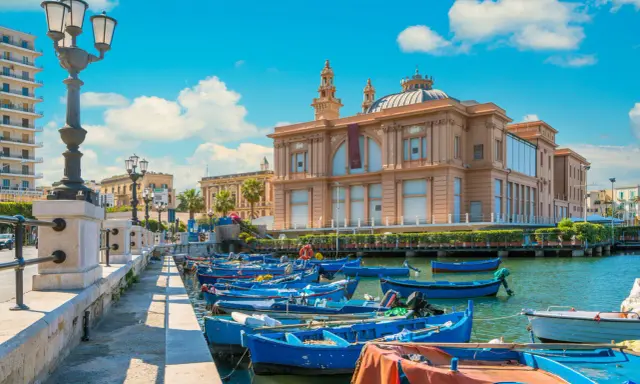 Barche blu ormeggiate nel porto di Bari, con il Teatro Margherita sullo sfondo. Un'immagine che cattura l'essenza di cosa vedere a Bari.