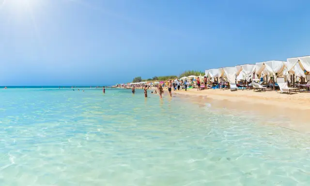 Spiaggia pugliese con acque cristalline e lettini sotto gazebo bianchi, ideale località mare Puglia per famiglie.