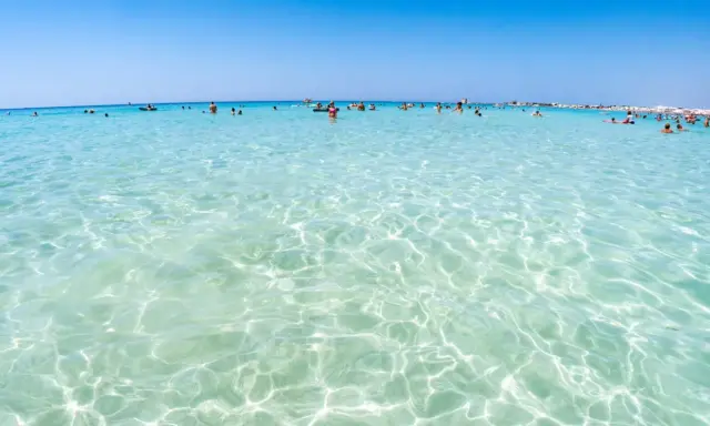 Acque cristalline e turchesi bagnano le spiagge di Lecce, dove bagnanti si godono il sole e il mare limpido.