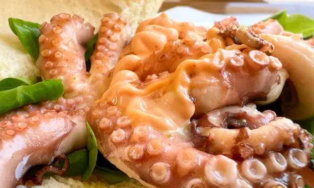 Tentacoli di polpo succulenti, un assaggio della sagra del polpo a Melendugno, serviti con pane croccante e foglie verdi.