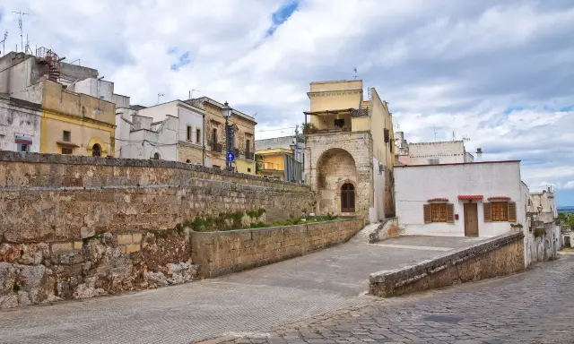 Antica strada di Ugento, dove si trova questo scorcio di case storiche con un muro in pietra grezza e un arco in tufo.