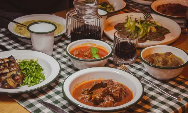 Tavola imbandita in una trattoria tipica salentina con vari piatti di carne e contorni, accompagnati da vino rosso.