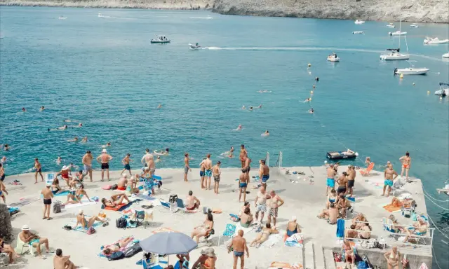 Gente in spiaggia e in mare a Santa Maria di Leuca, con barche all'orizzonte.