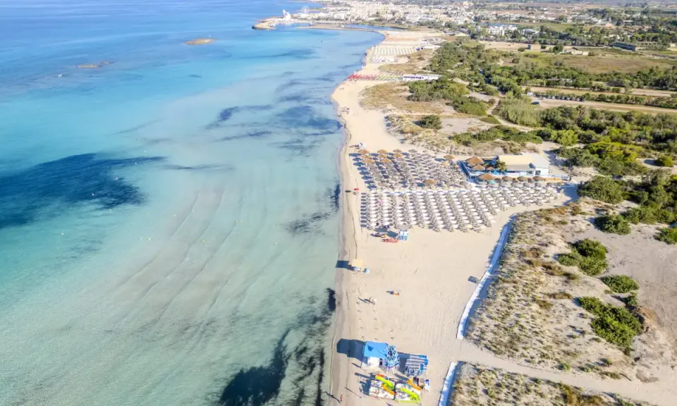 Spiaggia di Torre San Giovanni con ombrelloni e lettini, mare cristallino e vegetazione mediterranea.