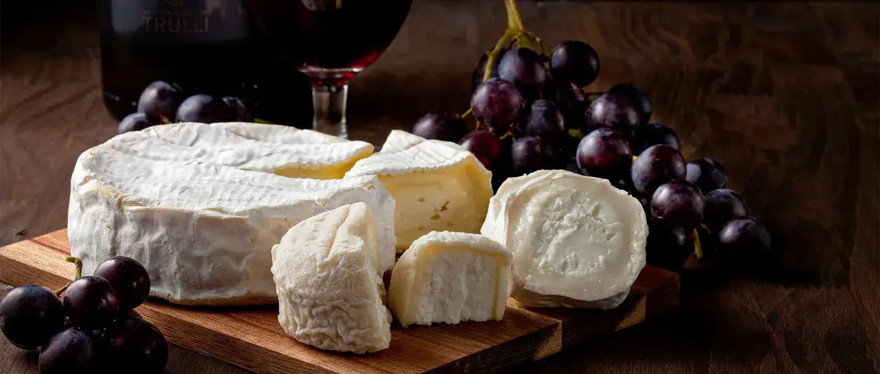 Formaggi pugliesi e uva nera, con una bottiglia di vino rosso sullo sfondo.
