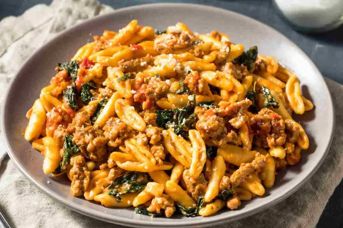 Piatto di pasta salentina con sugo di salsiccia e verdure, cosparso di formaggio grattugiato.