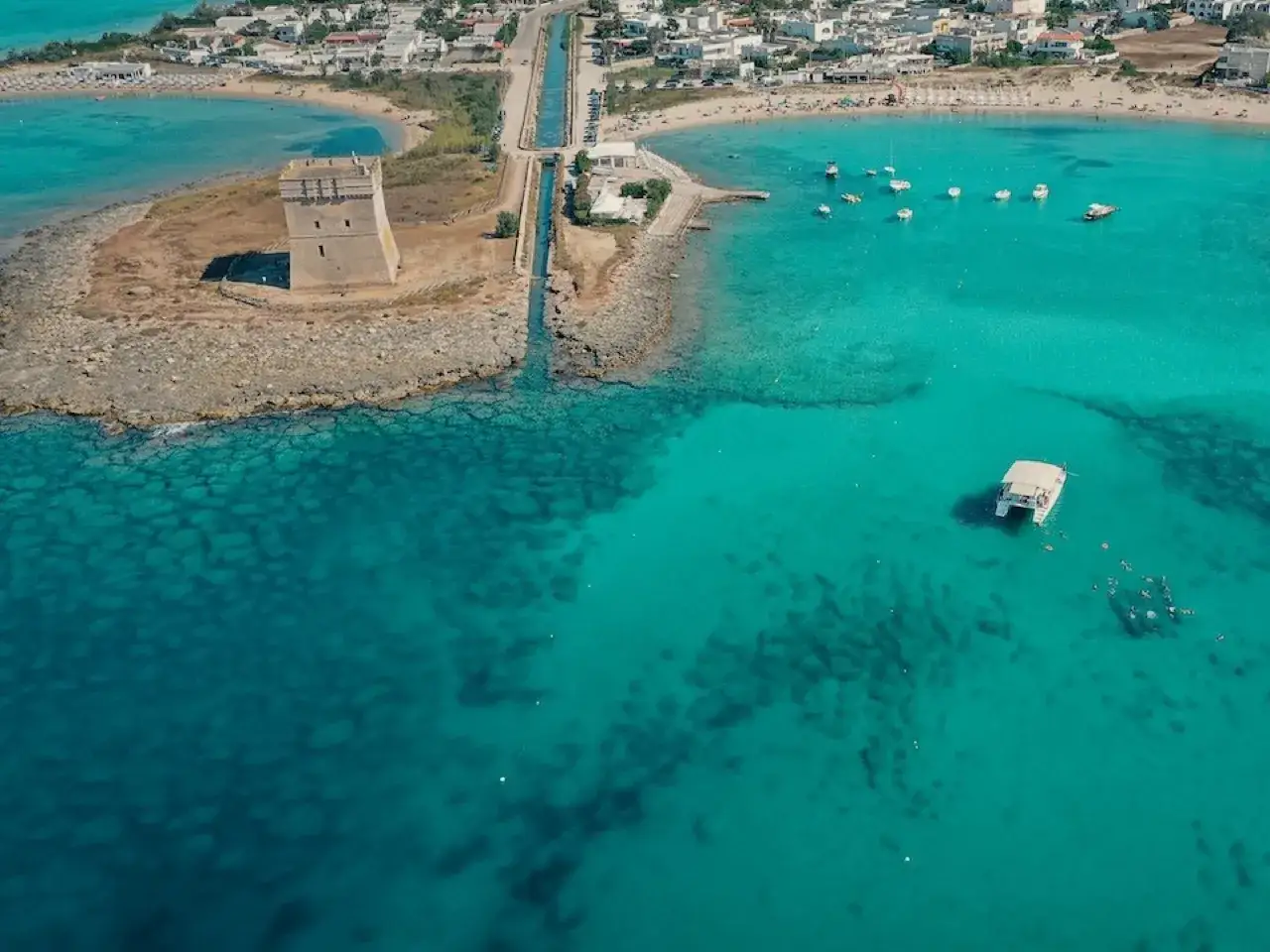 Torre Lapillo, una torre antica su una spiaggia caraibica con acque cristalline e un catamarano.